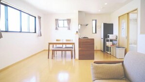 A room with a sofa, a dining table with chairs, a kitchen area with a microwave, and a wooden cabinet. - DUO ‧ OKINAWA (Onna)