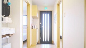 A hotel hallway with a door at the end, a trash bin, and a shelf with folded towels. - DUO ‧ OKINAWA (Onna)