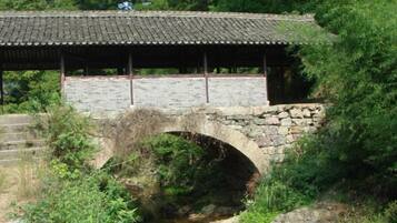 A stone bridge with a tiled roof over a stream, surrounded by greenery.