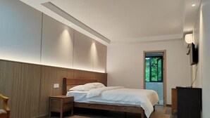 A modern bedroom with a wooden bed, bedside tables, a TV, and a view of greenery through a window.
