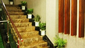 A staircase with potted plants on each step, a wooden handrail, and a wall with vertical blinds. - Ming Dian Hotel (Shaoshan)