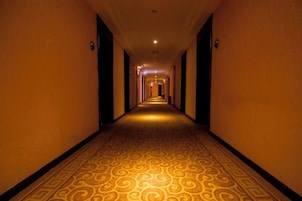 Pasillo de hotel con alfombra estampada, puertas a ambos lados y una lámpara en el techo.