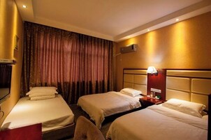 Habitación de hotel con dos camas individuales, una mesita de noche con lámpara, un equipo de aire acondicionado en la pared y un ventanal con cortinas.