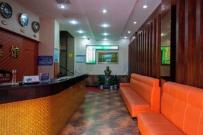 A reception area with a reception desk, a sofa, and a wall with clocks and a framed picture. - Ming Dian Hotel (Shaoshan)