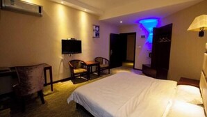 A hotel room with a bed, a desk, a chair, a TV, and a bathroom with a blue light. - Ming Dian Hotel (Shaoshan)
