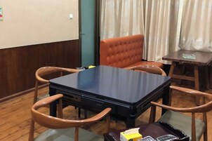 Una habitación con una mesa de madera oscura, cuatro sillas de madera, una mesita auxiliar de madera y una maleta en el suelo.