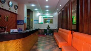 Una zona de recepción con mostrador, un área de espera con asientos naranjas y un reloj fijado a la pared.