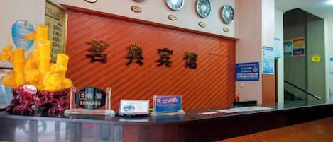 A hotel reception desk with a tiled counter, a reception desk sign, and a wall clock.