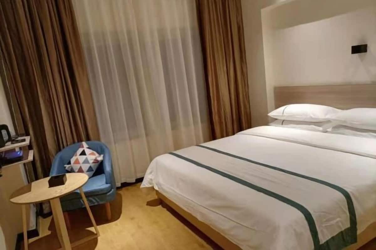 A hotel room with a bed, a small table, a chair, and a desk with a computer.