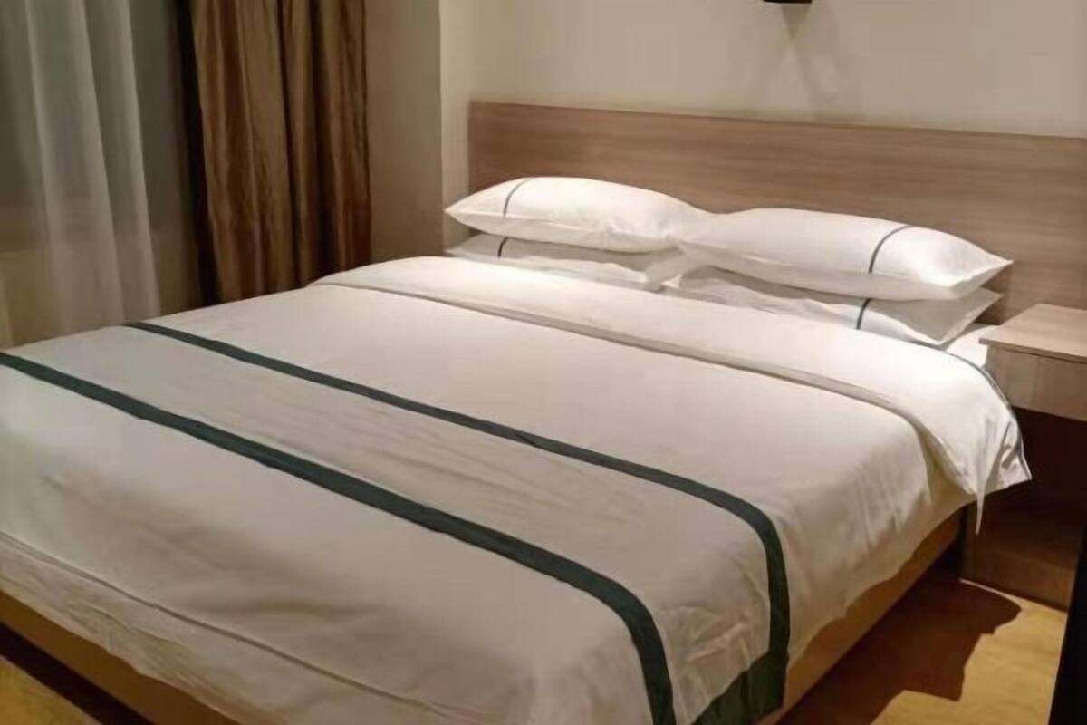 A neatly made bed with white bedding and green stripes, a wooden headboard, and a bedside table with a lamp.