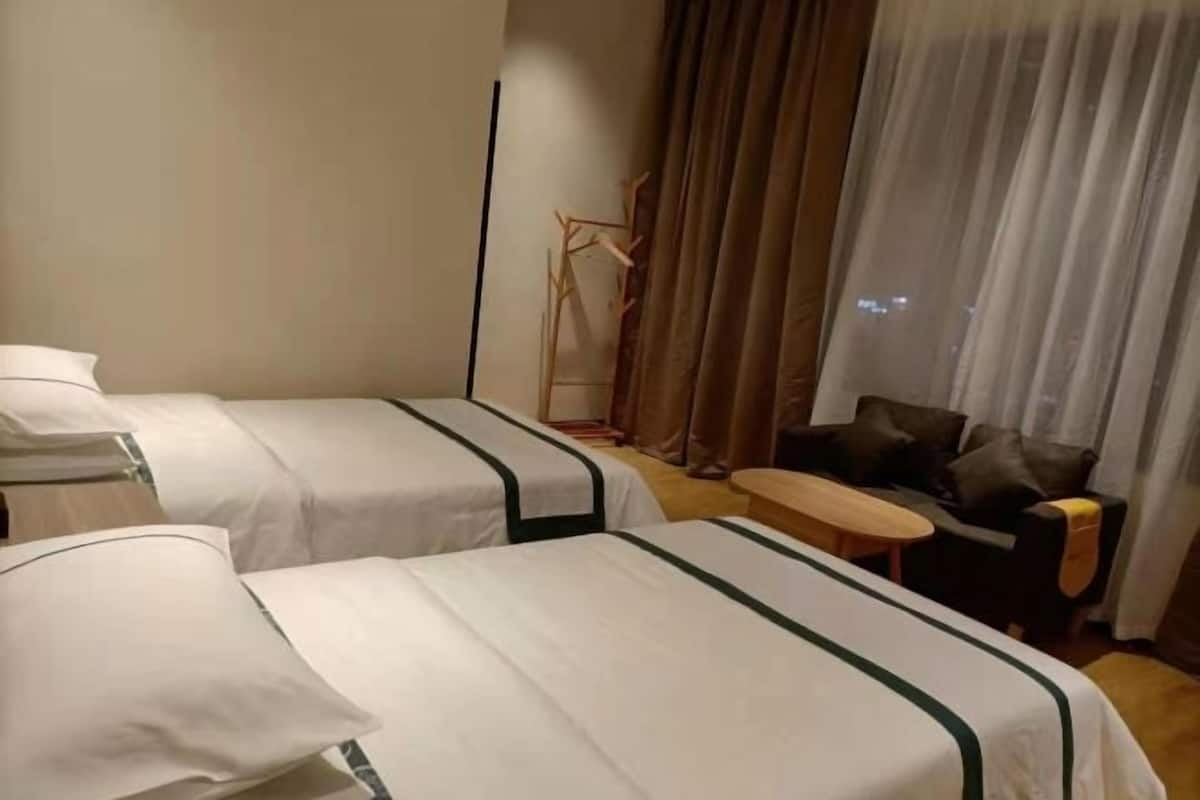 A hotel room with two beds, a small round table, a sofa, and a window with curtains.