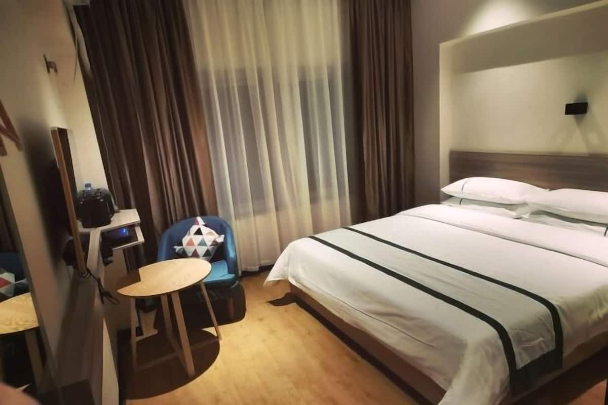 A hotel room with a bed, a desk, a chair, and a curtain.