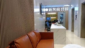 A modern hotel lobby with a leather sofa, a marble reception desk, and a television mounted on the wall. - Sunshine Express Hotel(Haikou international trade store) (Haikou)