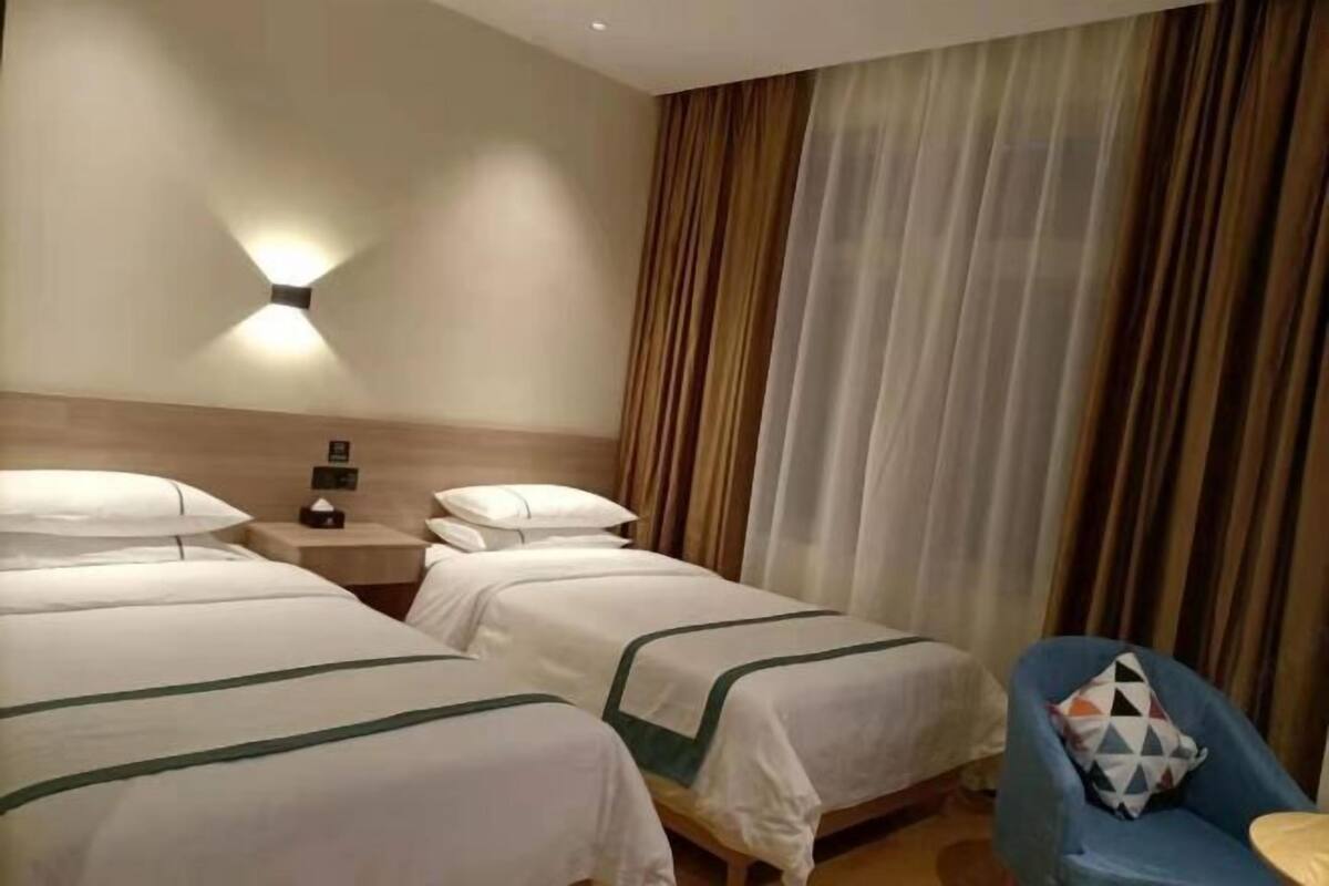 A hotel room with two beds, a nightstand, a lamp, a chair, and a window with curtains.