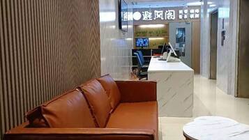 A modern hotel lobby with a leather sofa, a round table, and a reception desk.