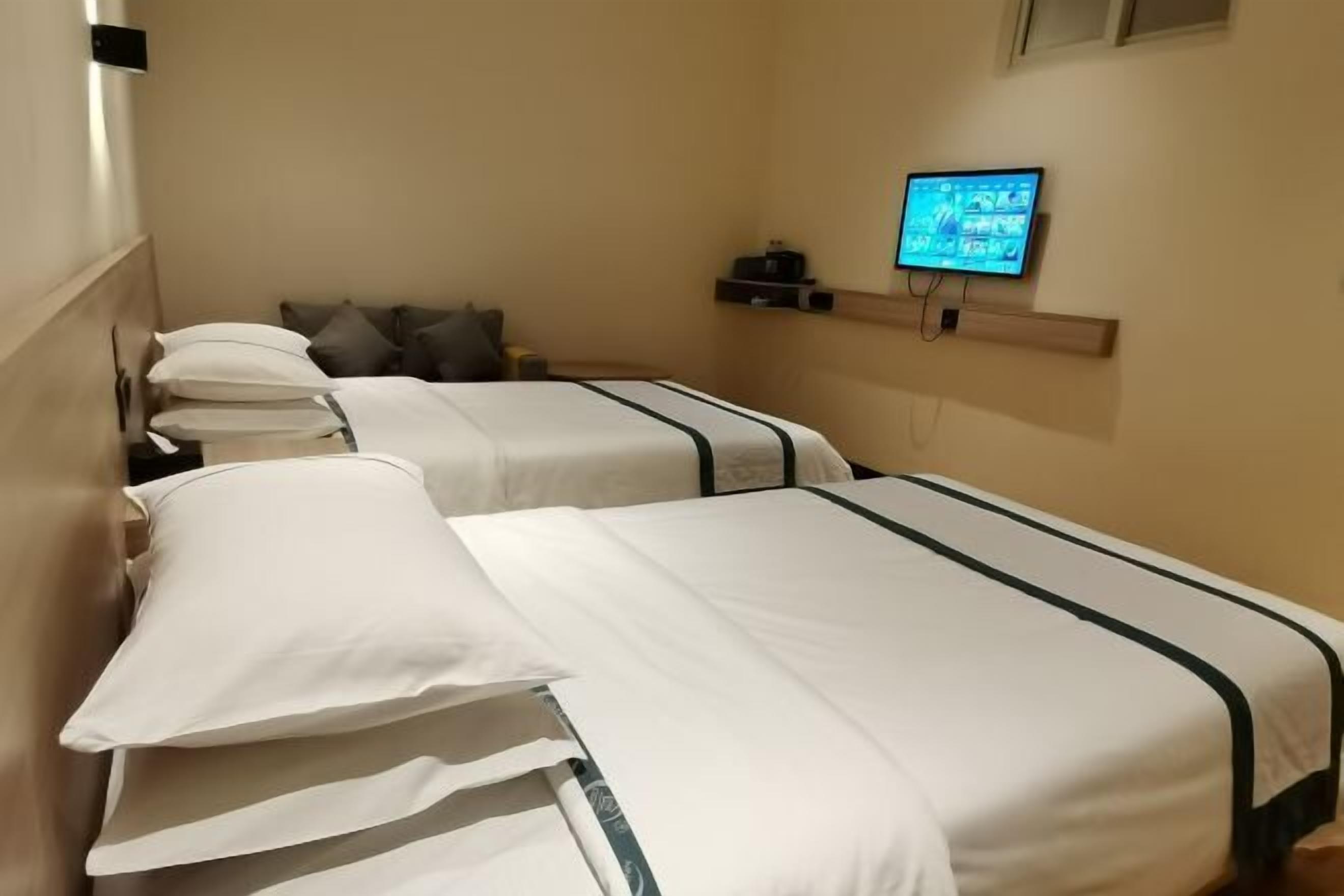 Habitación de hotel con dos camas, un televisor montado en la pared y una pequeña estantería con objetos.