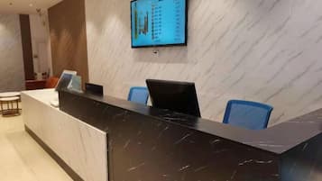 A hotel reception desk with a digital display, a marble counter, and blue chairs.