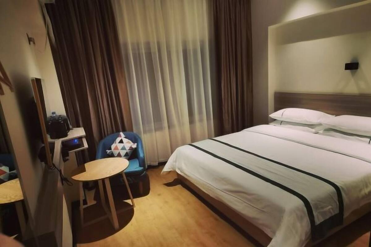 A hotel room with a bed, a desk, a chair, and a curtain.