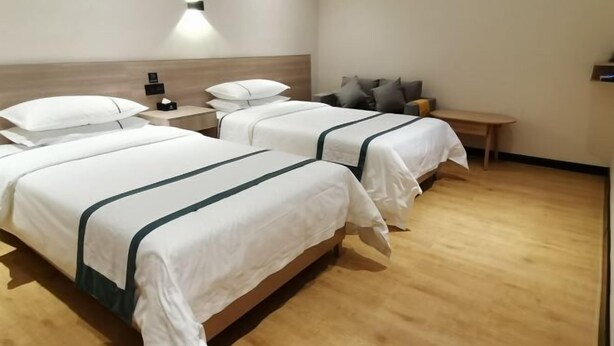A hotel room with two beds, a bedside table with a lamp, a bench, and a wall-mounted light fixture. - Sunshine Express Hotel(Haikou international trade store) (Haikou)