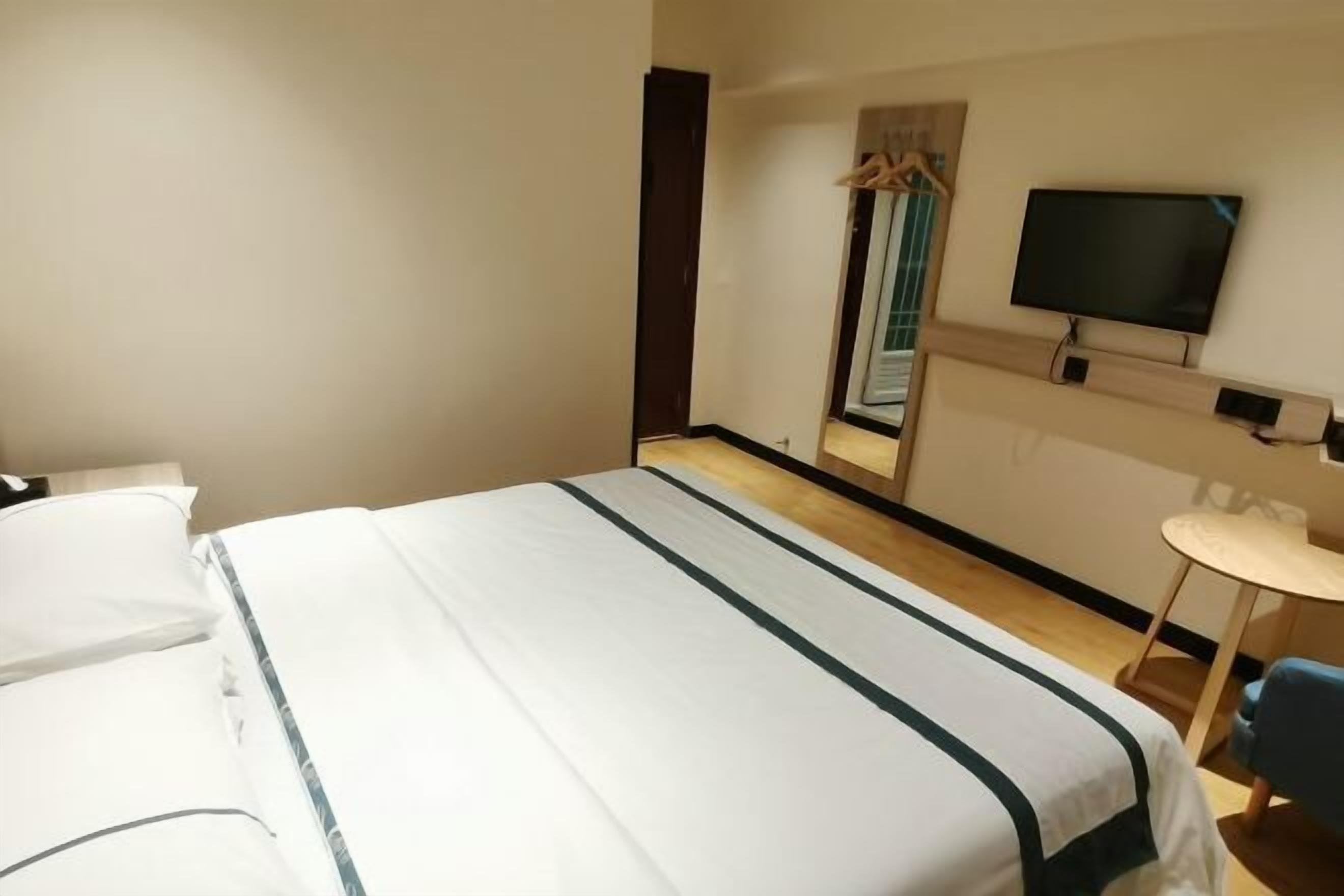 Una habitación de hotel con una cama, televisión, una mesita y un espejo.
