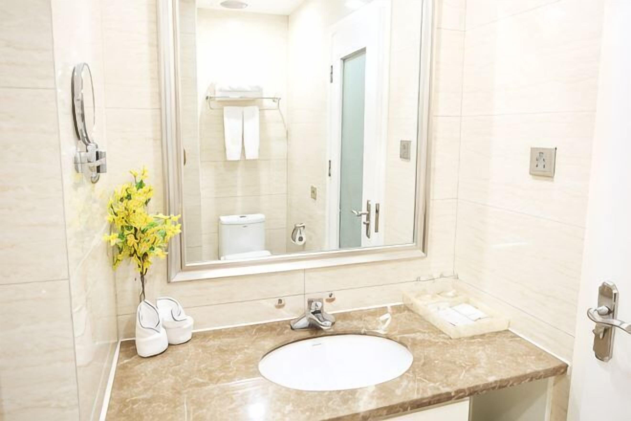 A bathroom with a white sink, a large mirror, and a vase with yellow flowers.