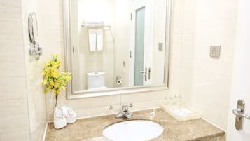 A bathroom with a white sink, a large mirror, and a vase with yellow flowers.