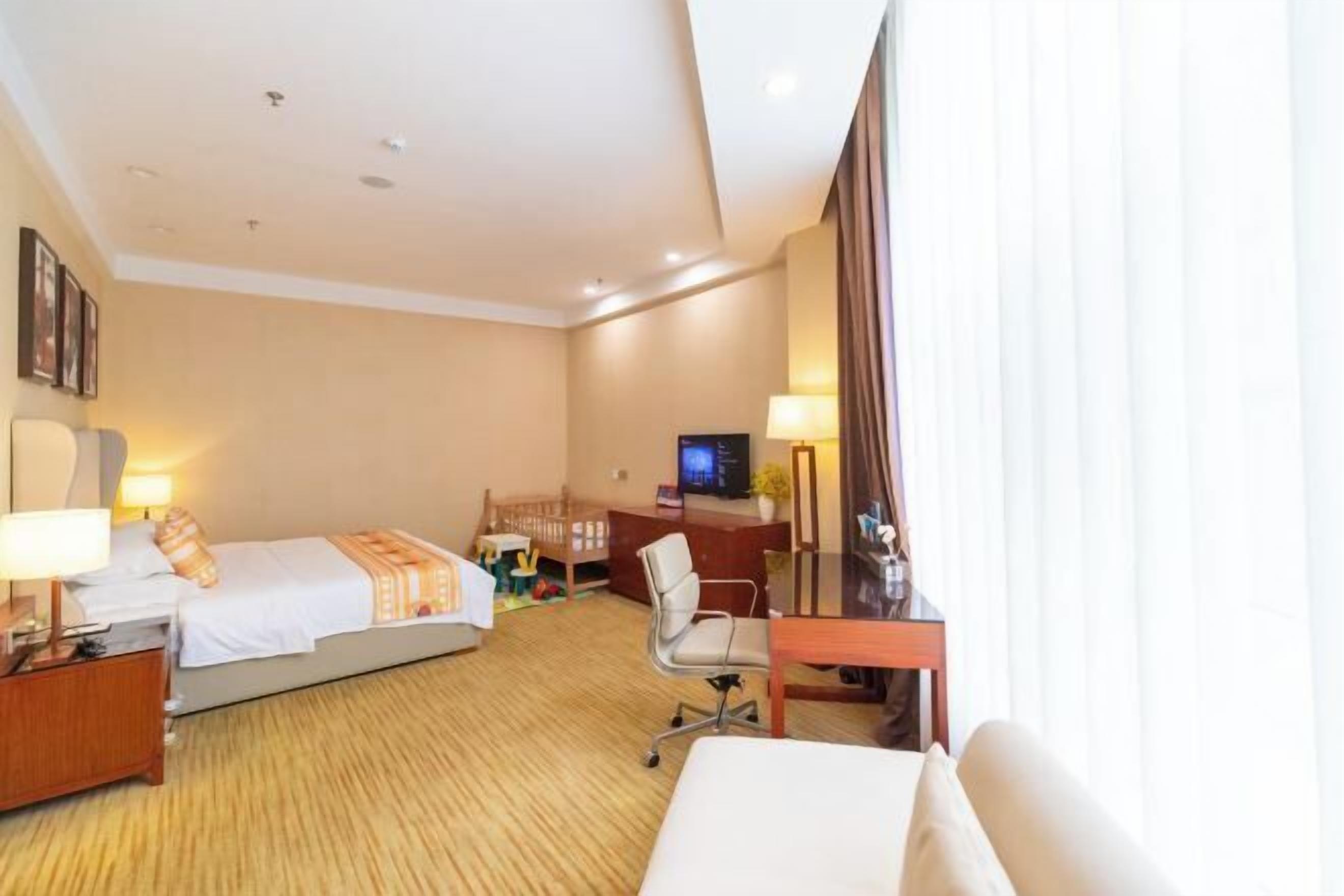 Ein Hotelzimmer mit zwei Betten, einem Schreibtisch, einem Sessel, einem Fernseher und einem Fenster mit Vorhängen.