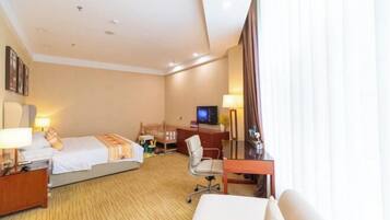 Ein Hotelzimmer mit zwei Betten, einem Schreibtisch, einem Sessel, einem Fernseher und einem Fenster mit Vorhängen.