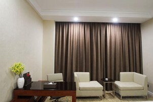 Una habitación de hotel con cama, escritorio, dos sillas y ventana con cortinas.