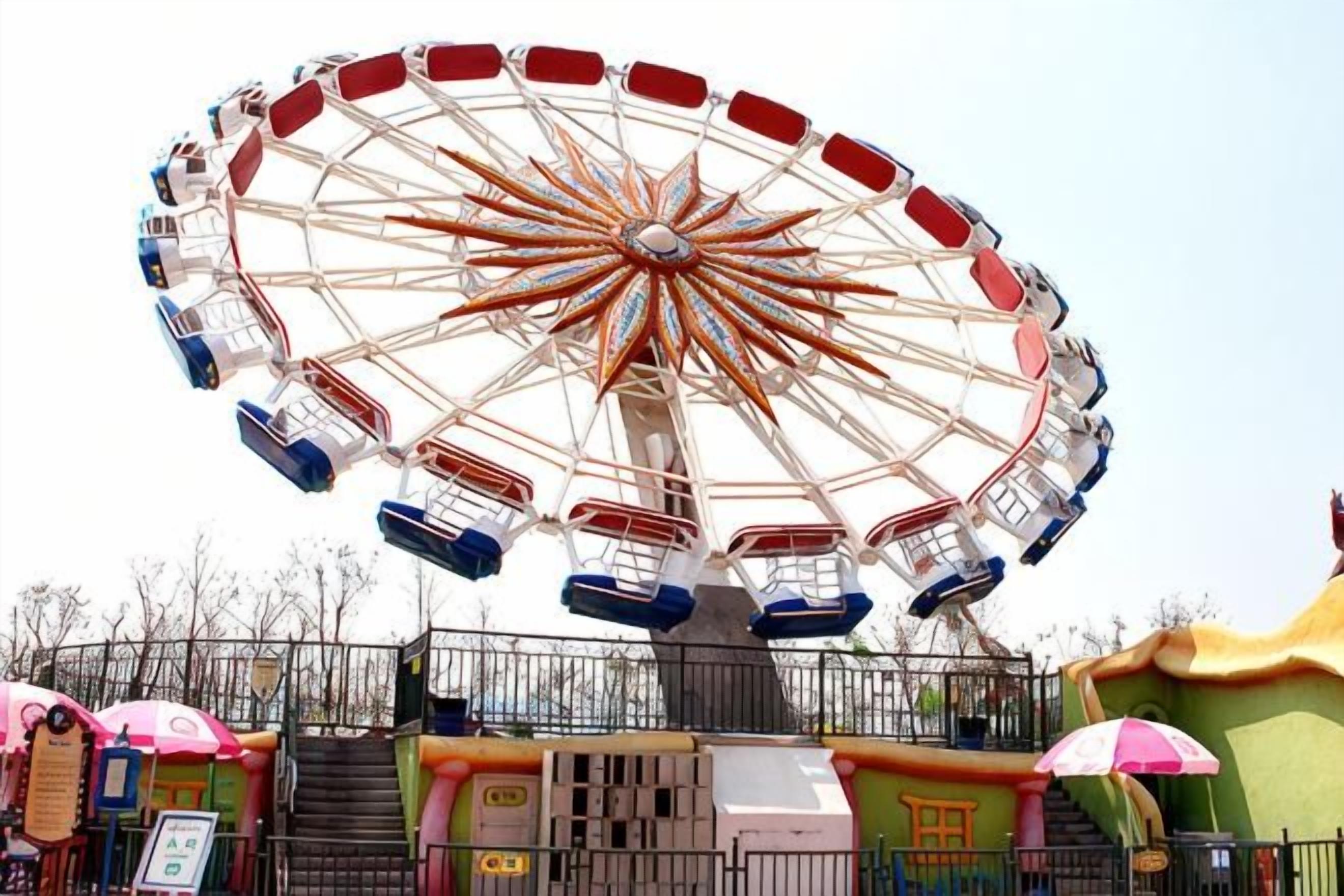 A Ferris wheel with cabins, a fenced area, and a colorful building structure.