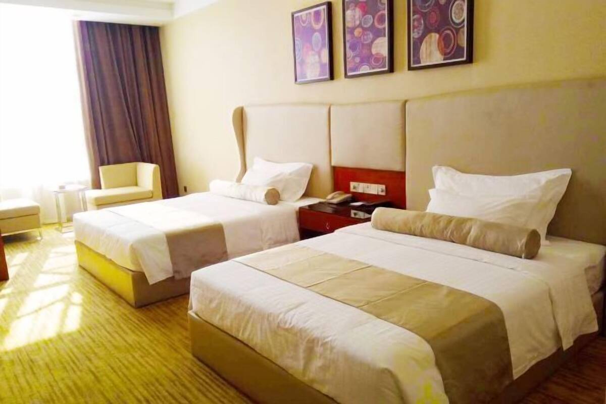Une chambre d’hôtel avec deux lits, une table de chevet avec une lampe, une chaise et des œuvres d’art accrochées au mur.