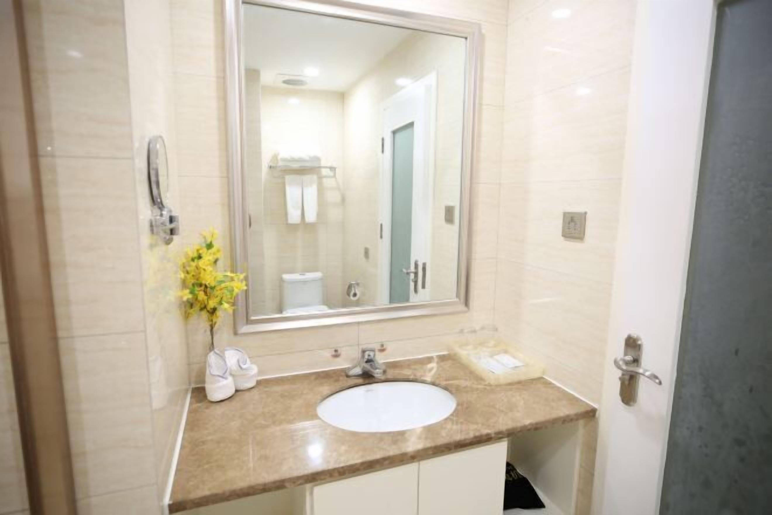 A bathroom with a large mirror, white sink, and a vase with yellow flowers.