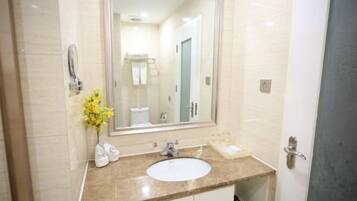 A bathroom with a large mirror, white sink, and a vase with yellow flowers.