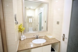Casa de banho com um espelho grande, lavatório branco e um vaso com flores amarelas.