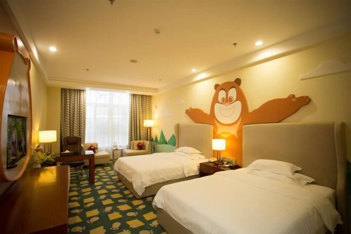 Une chambre d’hôtel avec deux lits, un bureau, une chaise, un grand dessin de personnage de dessin animé sur le mur et une fenêtre avec des rideaux.