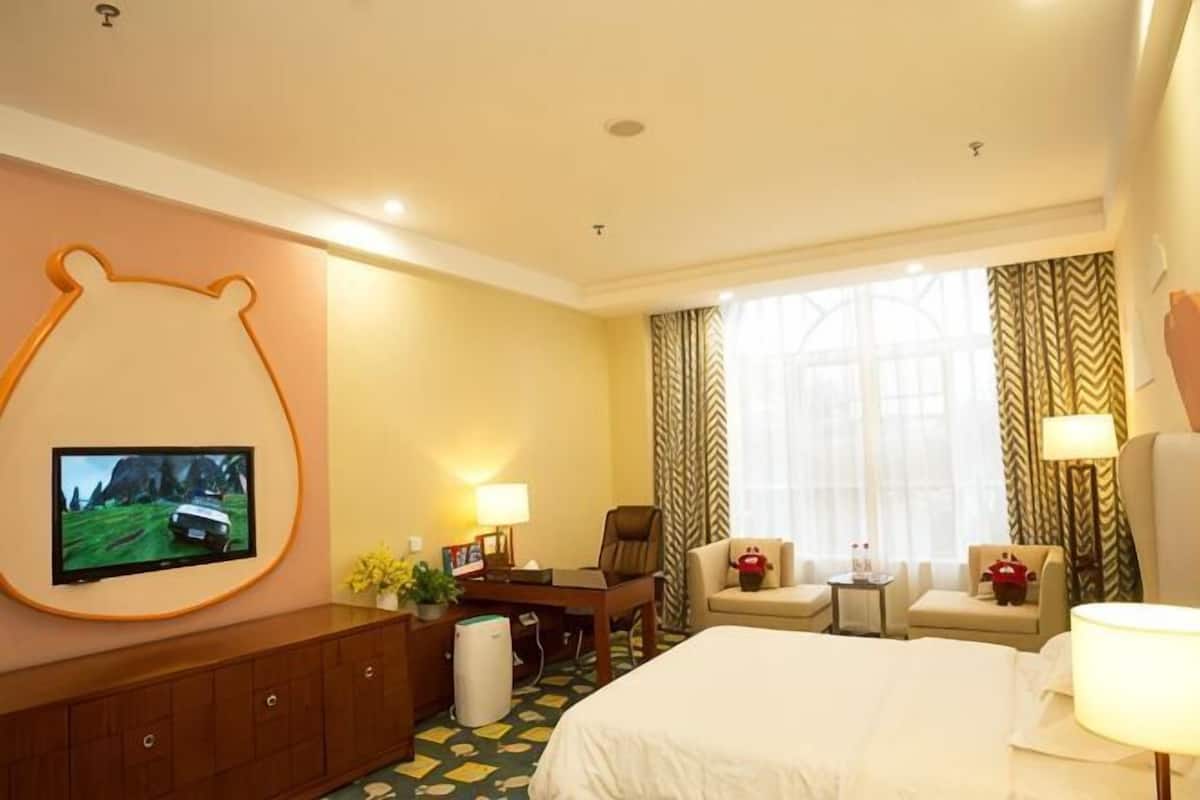 Une chambre d’hôtel comprenant un lit, un téléviseur fixé au mur, un bureau avec une chaise et une petite table avec une lampe.