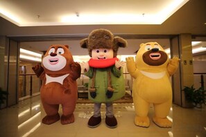 Three mascots standing in a lobby with a glass door and a plant in the background.