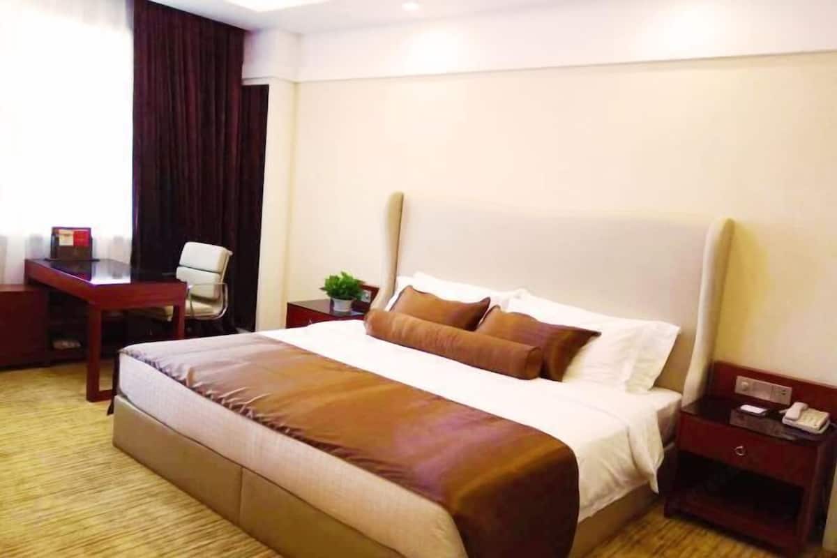 Une chambre d’hôtel avec un grand lit, un bureau, une chaise, une table de chevet et un rideau.