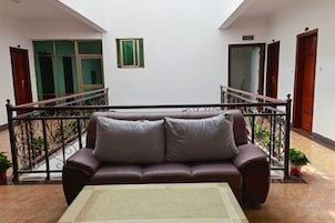 Un sofá de cuero marrón con cojines en una habitación con piso de baldosas, barandilla de metal y una puerta al fondo.