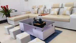 A modern living room with a sectional sofa, a glass coffee table, and white poufs. - Wenchang Ruyi Hotel (Wenchang)
