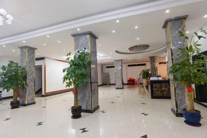 Un vestíbulo de hotel con pilares de mármol, plantas en macetas y un mostrador de recepción.