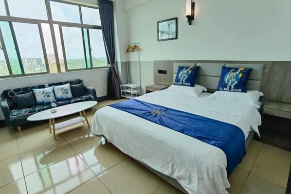 A hotel room with a large bed, a sofa, a small table, and a view of the outside.