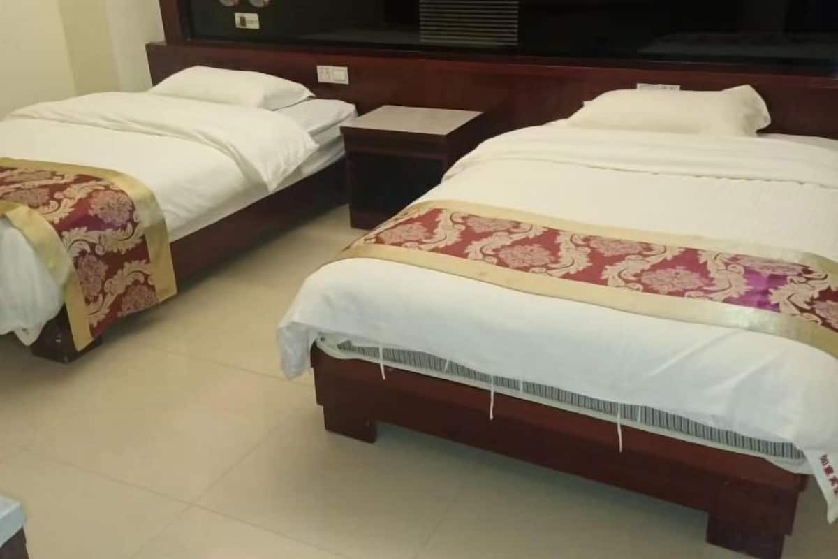 Ein Hotelzimmer mit zwei Einzelbetten und einem größeren Bett, alles mit weißen Leinen und dekorativen Kopfteilen.