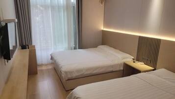 A hotel room with two beds, a desk, a TV, and a window with curtains.