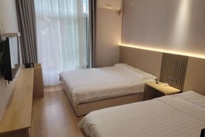 A hotel room with two beds, a desk, a TV, and a window with curtains.