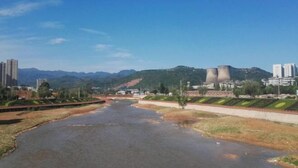 Un río serpentea por una ciudad con edificios industriales y montañas al fondo.