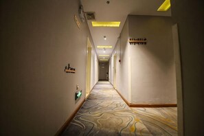 Um corredor de hotel com carpete estampado, placas fixadas na parede e iluminação embutida.