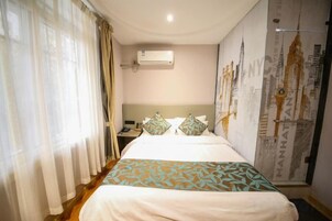 Habitación de hotel con cama, cortinas, aire acondicionado, mesita de noche y una pared con una obra de arte urbana.