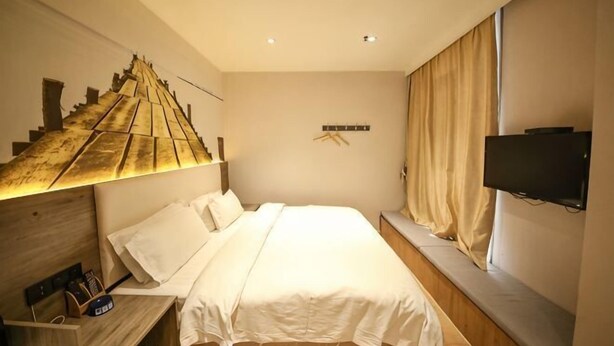 Habitación de hotel con cama, televisión montada en la pared, escritorio con silla y ventana con cortinas.