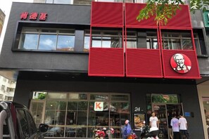 A building with a red and black facade, a KFC sign, and a visible entrance with people outside.